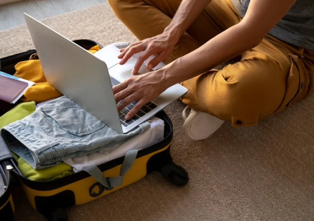 Mulher mexendo no notebook, que está em cima de uma mala.