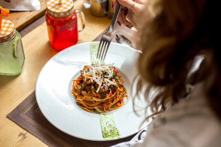 Vista lateral, uma menina come espaguete com carne e queijo ralado.