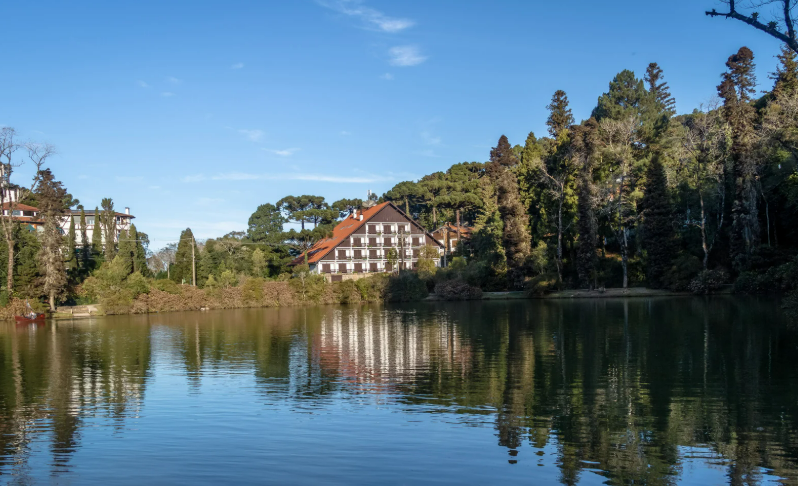 Paisagem do Lago Negro cercado por araucárias e prédio em estilo europeu refletido na água representando o charme da Serra Gaúcha